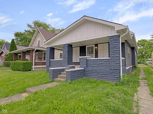 1411 N Grant Ave, Indianapolis, IN 46201 - view of front of house with covered porch, board and batten siding, a front lawn, and stone siding