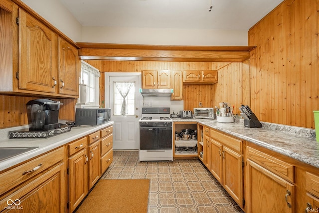 2007 Lincoln Ave, New Castle, IN 47362 - kitchen with white gas stove, under cabinet range hood, light countertops, light floors, and wood walls