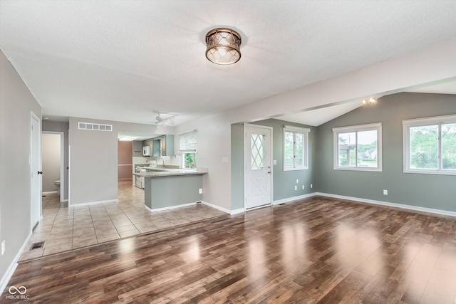 8205 Picadilly Ln, Indianapolis, IN 46256 - unfurnished living room featuring light wood finished floors, a sink, lofted ceiling, baseboards, and a textured ceiling