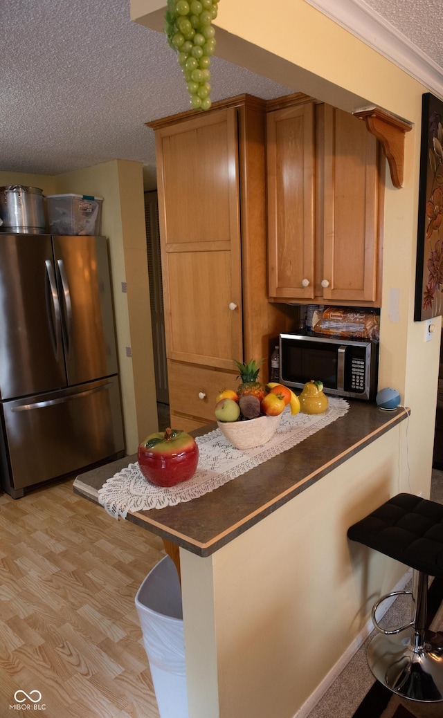 7402 Broadview Dr, Indianapolis, IN 46227 - kitchen featuring appliances with stainless steel finishes, a textured ceiling, brown cabinets, dark countertops, and a breakfast bar