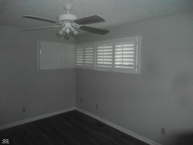 spare room with baseboards, dark wood-style flooring, and a ceiling fan