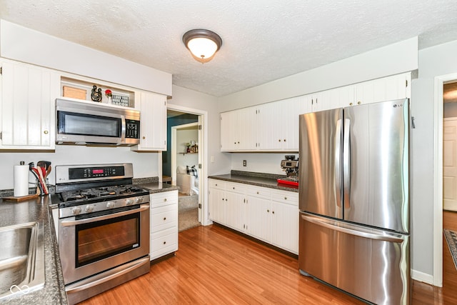 6580 Kings Ct, Avon, IN 46123 - kitchen with stainless steel appliances, dark countertops, light wood-style flooring, white cabinetry, and a textured ceiling