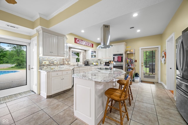 5439 E Kinderhook Rd, Scottsburg, IN 47170 - kitchen featuring island exhaust hood, a kitchen bar, decorative backsplash, stainless steel appliances, and light stone counters