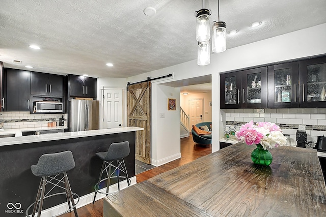 1548 N Park Ave, Indianapolis, IN 46202 - kitchen with appliances with stainless steel finishes, dark cabinetry, a barn door, a breakfast bar area, and dark wood-type flooring