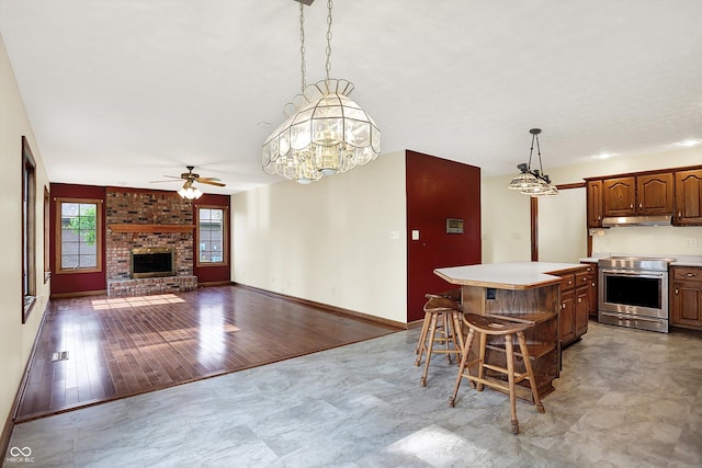 8619 Wrangler Ct, Indianapolis, IN 46217 - kitchen with stainless steel range with electric stovetop, under cabinet range hood, ceiling fan, a brick fireplace, and light countertops
