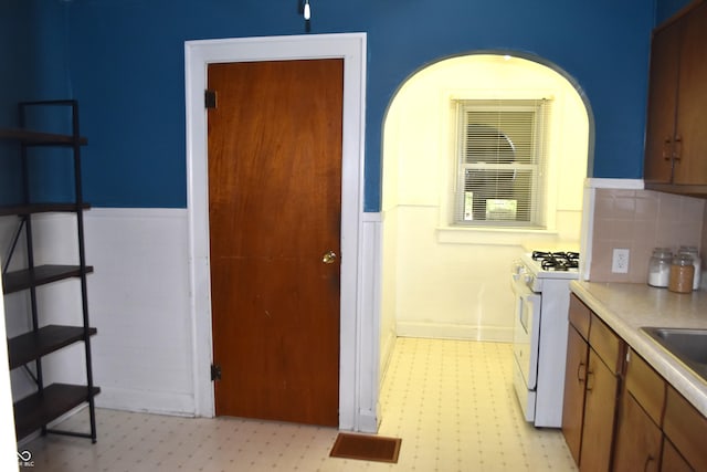1641 Winton Ave, Speedway, IN 46224 - kitchen with white gas stove, wainscoting, light flooring, light countertops, and brown cabinetry