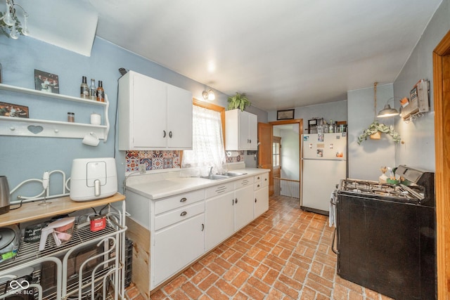 3004 Sheridan St, Anderson, IN 46016 - kitchen with freestanding refrigerator, range with gas stovetop, brick flooring, light countertops, and white cabinets