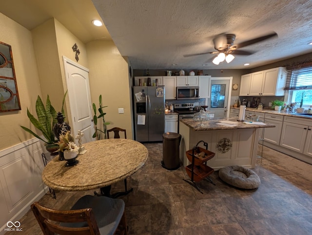 317 Washington St, Clay City, IN 47841 - kitchen with stainless steel appliances, white cabinetry, a ceiling fan, a kitchen island with sink, and stone countertops
