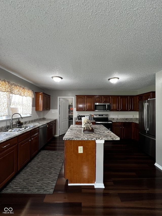 585 Fireside Dr, Greenwood, IN 46143 - kitchen featuring stainless steel appliances, a kitchen island, dark wood-type flooring, a textured ceiling, and light stone countertops
