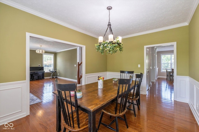 12772 Tram Ln, Carmel, IN 46032 - dining area with wainscoting, dark wood-style flooring, ornamental molding, a decorative wall, and a chandelier