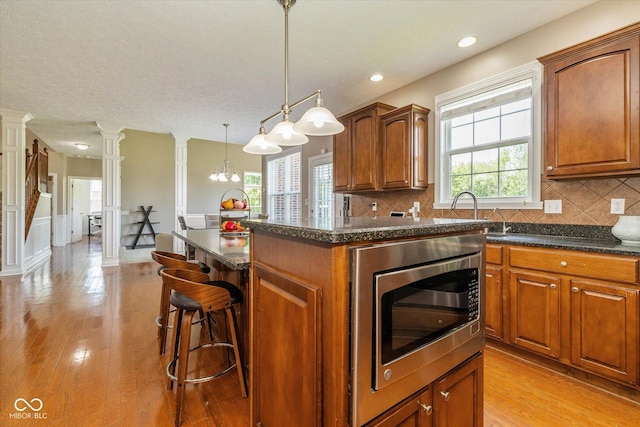 12772 Tram Ln, Carmel, IN 46032 - kitchen with stainless steel microwave, ornate columns, decorative backsplash, light wood-style flooring, and recessed lighting