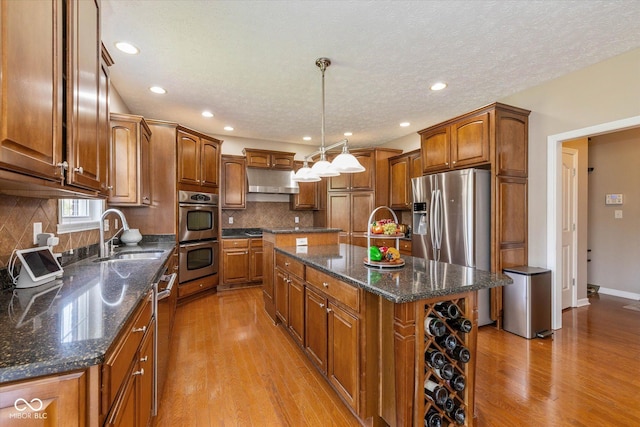 12772 Tram Ln, Carmel, IN 46032 - kitchen with appliances with stainless steel finishes, a center island, light wood-style floors, brown cabinetry, and a textured ceiling