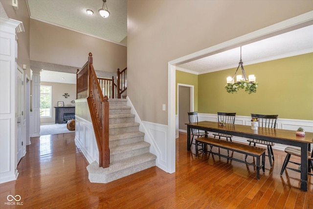 12772 Tram Ln, Carmel, IN 46032 - staircase featuring a tile fireplace, wood finished floors, ornamental molding, a wainscoted wall, and a chandelier