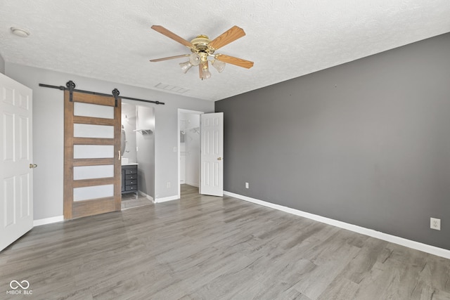 10693 Newgate Ln, Indianapolis, IN 46231 - unfurnished bedroom featuring a barn door, wood finished floors, baseboards, and a textured ceiling