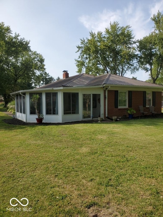 1322 Greenway Dr, Anderson, IN 46011 - rear view of house featuring a sunroom, a chimney, a lawn, and metal roof