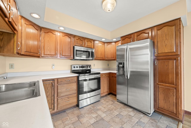 1105 Sarah Ct, Greenwood, IN 46142 - kitchen featuring appliances with stainless steel finishes, a sink, recessed lighting, brown cabinets, and light stone finish flooring