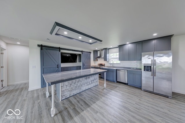 32 Downing Dr, Trafalgar, IN 46181 - kitchen with appliances with stainless steel finishes, wall chimney exhaust hood, a barn door, light wood finished floors, and tasteful backsplash