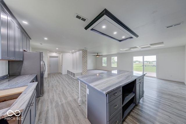 32 Downing Dr, Trafalgar, IN 46181 - kitchen featuring light wood-type flooring, gray cabinets, a center island, a ceiling fan, and light stone counters