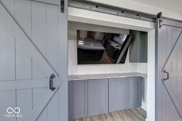 32 Downing Dr, Trafalgar, IN 46181 - kitchen featuring gray cabinets, a barn door, light wood finished floors, and light stone counters