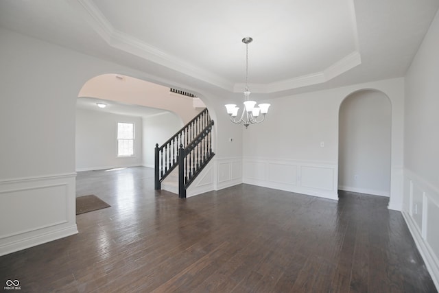 15201 Slateford Rd, Noblesville, IN 46062 - empty room featuring arched walkways, a tray ceiling, stairs, dark wood finished floors, and a wainscoted wall