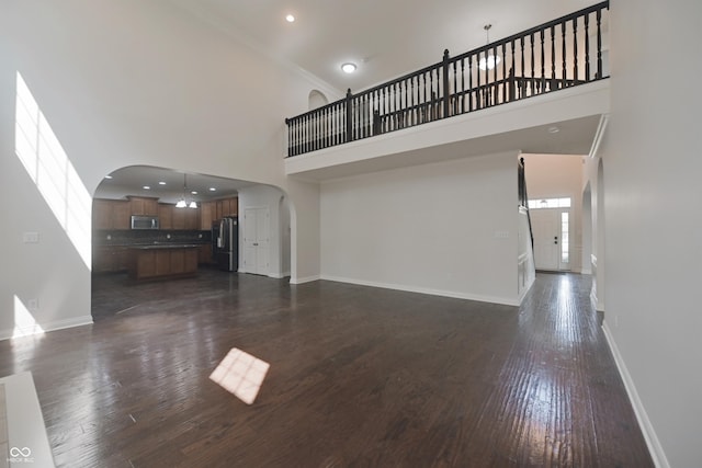 15201 Slateford Rd, Noblesville, IN 46062 - unfurnished living room featuring arched walkways, a towering ceiling, baseboards, dark wood-type flooring, and recessed lighting