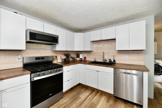 1445 Biloxi Ln, Beech Grove, IN 46107 - kitchen featuring appliances with stainless steel finishes, butcher block countertops, a textured ceiling, light wood-style floors, and washer / dryer