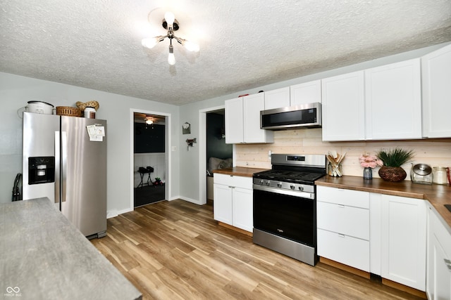 1445 Biloxi Ln, Beech Grove, IN 46107 - kitchen with appliances with stainless steel finishes, wooden counters, white cabinetry, light wood finished floors, and a textured ceiling