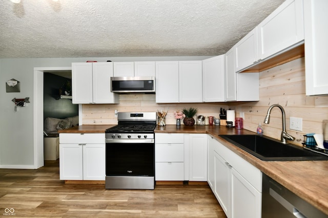 1445 Biloxi Ln, Beech Grove, IN 46107 - kitchen featuring appliances with stainless steel finishes, a textured ceiling, white cabinets, light wood-style flooring, and wood counters