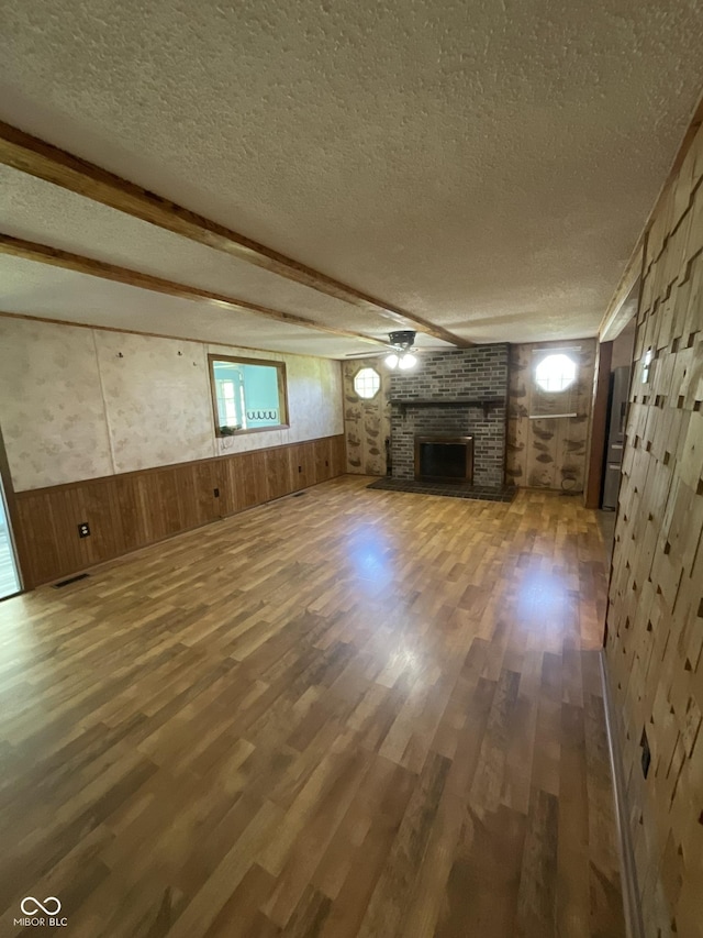 6758 S US Highway 63, Hillsdale, IN 47854 - unfurnished living room with a textured ceiling, wood walls, wood finished floors, a brick fireplace, and a wainscoted wall