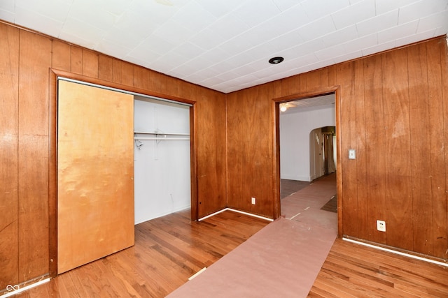 1346 W 27th St, Indianapolis, IN 46208 - unfurnished bedroom with arched walkways, wood finished floors, a closet, and wooden walls