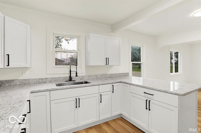 701 E Memorial Dr, Muncie, IN 47302 - kitchen featuring a sink, a peninsula, beam ceiling, light wood finished floors, and white cabinetry
