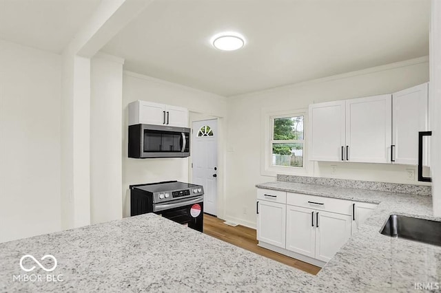 701 E Memorial Dr, Muncie, IN 47302 - kitchen with stainless steel appliances, wood finished floors, light stone countertops, white cabinetry, and crown molding