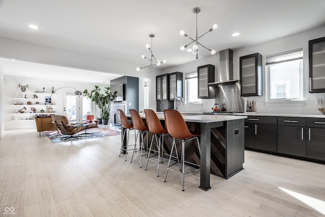 1622 Cornell Ave, Indianapolis, IN 46202 - kitchen featuring wall chimney range hood, a chandelier, an island with sink, a breakfast bar area, and glass insert cabinets