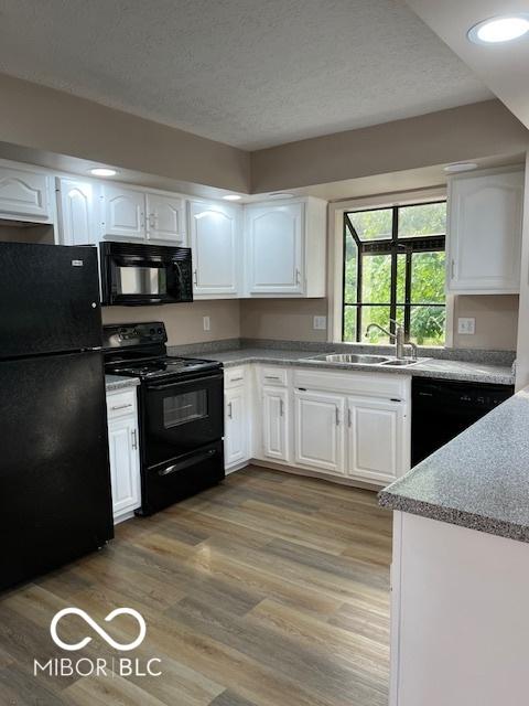 7707 River Rd Unit 10, Indianapolis, IN 46240 - kitchen with black appliances, a sink, white cabinets, light wood finished floors, and a textured ceiling