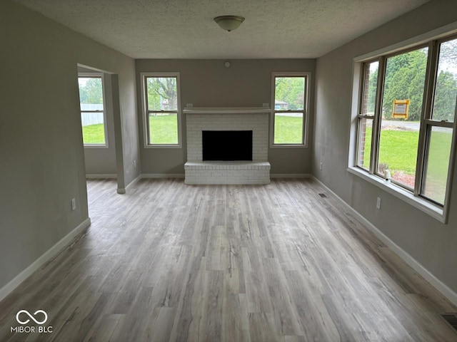 724 Iroquois St, Anderson, IN 46012 - unfurnished living room featuring wood finished floors, a textured ceiling, healthy amount of natural light, baseboards, and a brick fireplace