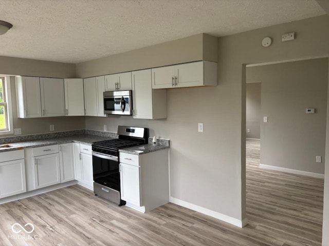 724 Iroquois St, Anderson, IN 46012 - kitchen with appliances with stainless steel finishes, light wood-type flooring, a textured ceiling, baseboards, and white cabinetry