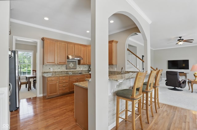 16802 Oak Manor Dr, Westfield, IN 46074 - kitchen with under cabinet range hood, freestanding refrigerator, ornamental molding, light wood finished floors, and light stone counters