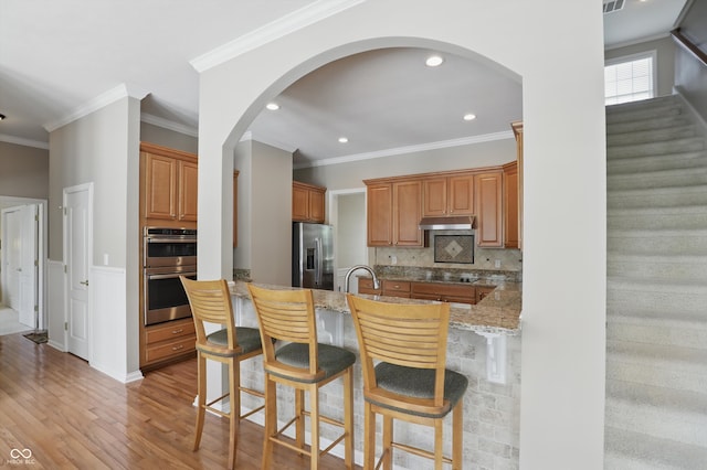 16802 Oak Manor Dr, Westfield, IN 46074 - kitchen with appliances with stainless steel finishes, a kitchen bar, light stone countertops, light wood finished floors, and crown molding