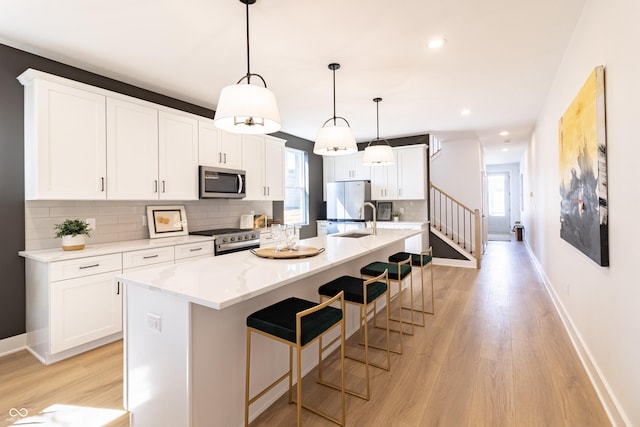 2051 Columbia Ave, Indianapolis, IN 46202 - kitchen featuring stainless steel appliances, light wood finished floors, backsplash, baseboards, and an island with sink