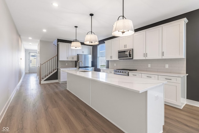 2053 Columbia Ave, Indianapolis, IN 46202 - kitchen featuring appliances with stainless steel finishes, a large island with sink, decorative backsplash, wood finished floors, and recessed lighting