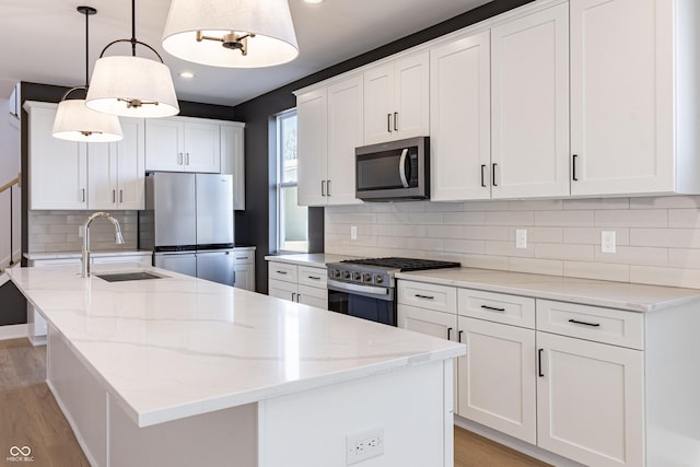 2053 Columbia Ave, Indianapolis, IN 46202 - kitchen featuring appliances with stainless steel finishes, a sink, a center island with sink, light wood-style floors, and decorative backsplash