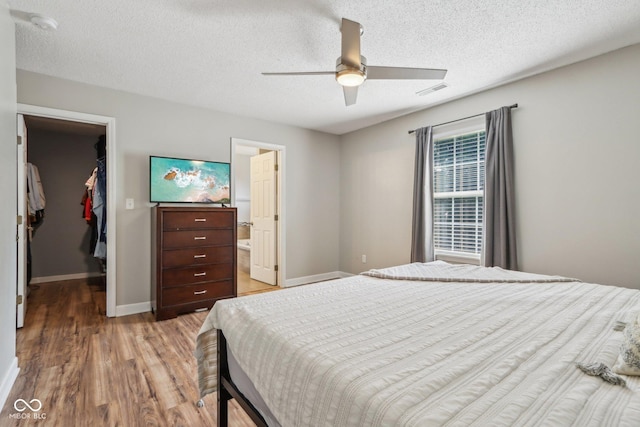 17357 Austrian Pine Way, Westfield, IN 46074 - bedroom featuring a walk in closet, light wood-style flooring, a closet, baseboards, and a textured ceiling