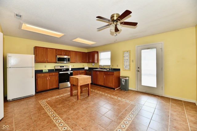 3429 Pavetto Ln, Indianapolis, IN 46203 - kitchen with stainless steel appliances, dark countertops, light tile patterned flooring, a ceiling fan, and brown cabinetry