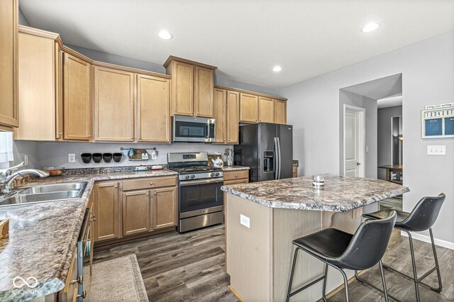 kitchen with appliances with stainless steel finishes, a sink, a kitchen island, a kitchen breakfast bar, and dark wood finished floors