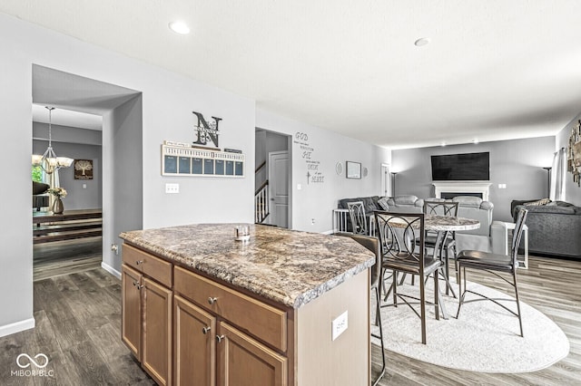 kitchen featuring dark wood-type flooring, a fireplace, a center island, and brown cabinetry