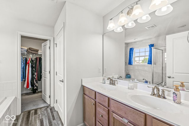 bathroom with a stall shower, wood finished floors, double vanity, a spacious closet, and tiled tub