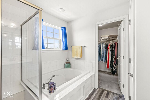 bathroom with a garden tub, a walk in closet, a shower stall, and wood finished floors