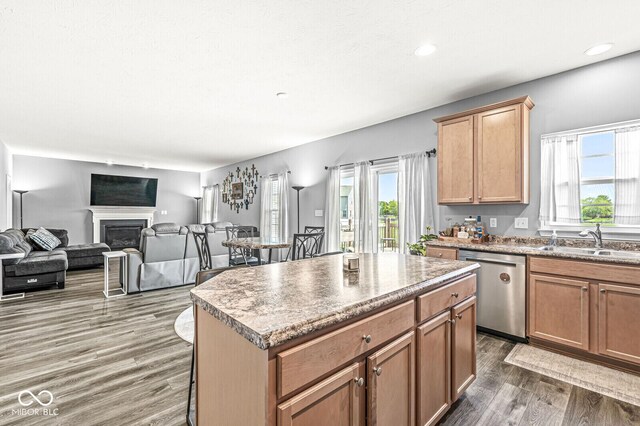 kitchen featuring stainless steel dishwasher, a sink, dark wood finished floors, a fireplace, and a kitchen island
