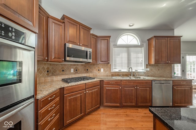 10555 Serra Vista Pt, Fishers, IN 46040 - kitchen with stainless steel appliances, a sink, light wood-style flooring, stone counters, and backsplash