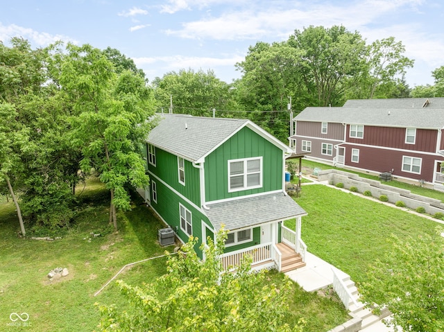 2427 N Rural St, Indianapolis, IN 46218 - view of front of house featuring board and batten siding, roof with shingles, covered porch, a front yard, and view of scattered trees